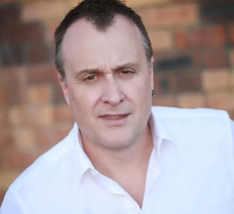 Darryl King standing in front of a brick wall wearing a white shirt and hoop earring
