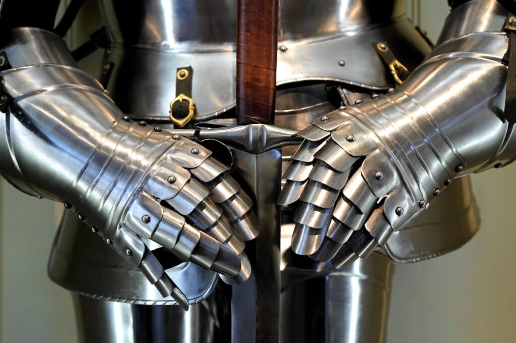A close-up of a shining suit of knight's armor with gauntleted hands gripping the hilt of a large, polished longsword, symbolizing heroism and battle in epic fantasy.
