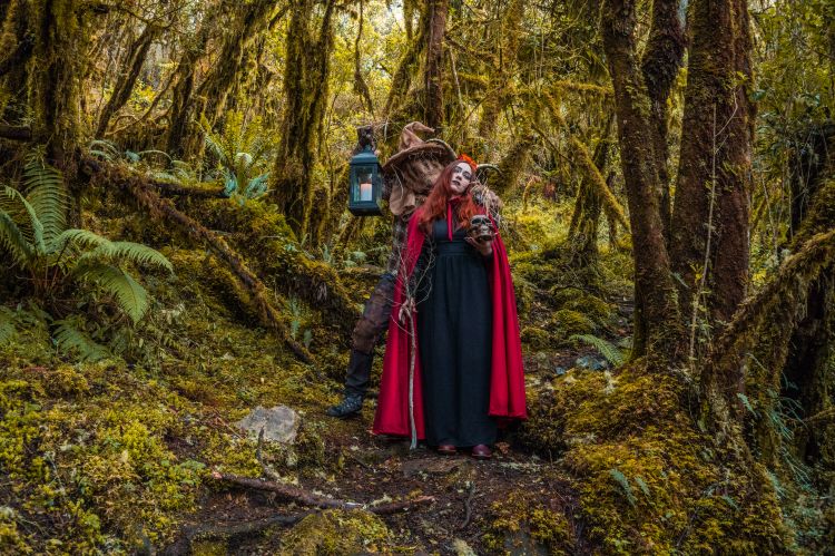 Two people in costume standing in a lush, mossy forest.