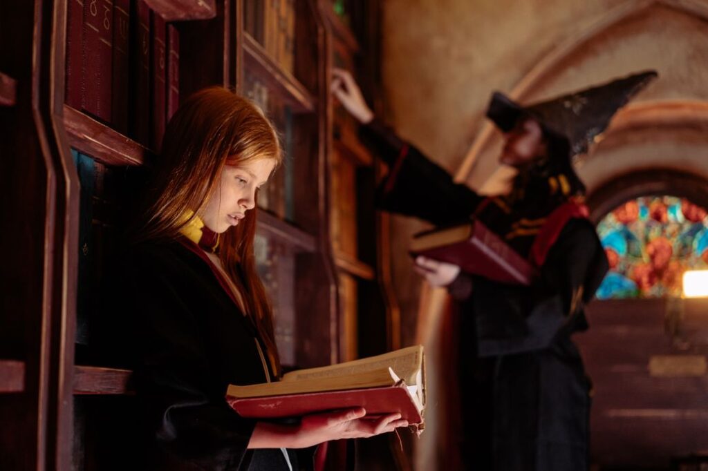 Two people in wizard robes reading books in a library.