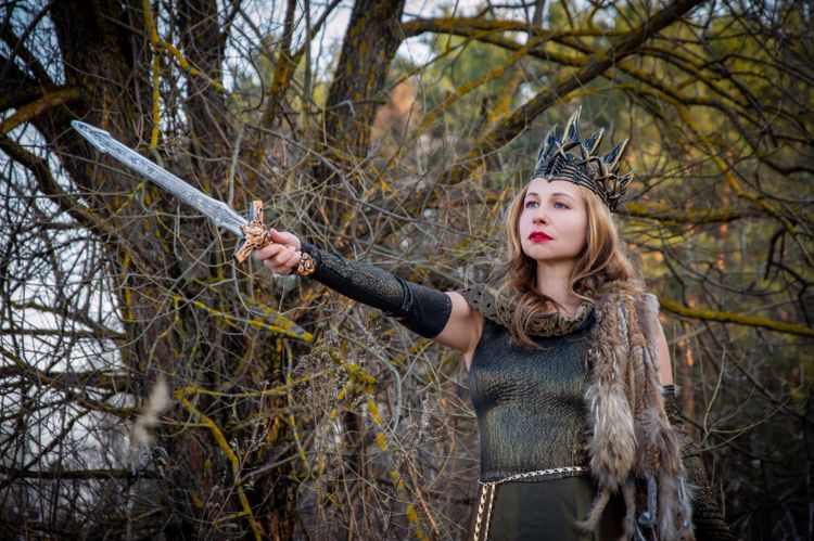 Woman in crown holding sword in forest setting.