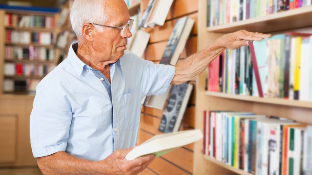 Elderly man in a library selecting a book from the shelf